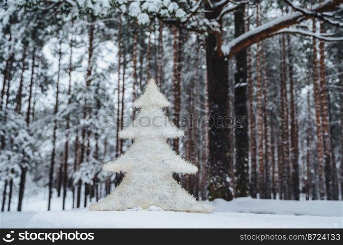Horizontal shot of artificial white New Year tree stands in winter forest against natural trees. Outdoor photo of Christmas white tree on beautiful nature