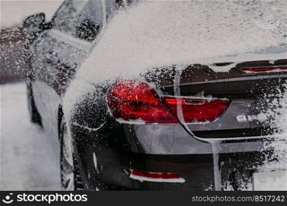 Horizontal shot of black car covered with soap. Cleanliness concept. Car washing concept. High pressure water. Automatic automobile wash