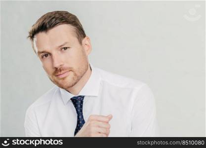 Horizontal shot of handsome young male entrepreneur in formal white shirt, looks directly at camera, listens attentively his interlocutor, talk on business theme, isolated over white background