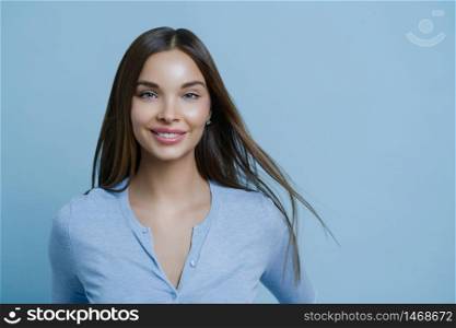 Horizontal shot of lovely woman has healthy beautiful hair, makeup, happy to get new job position, comes to interview, gets ready going out for romantic date, looks directly at camera, poses indoor