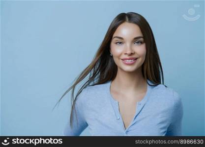Horizontal shot of lovely woman has healthy beautiful hair, makeup, happy to get new job position, comes to interview, gets ready going out for romantic date, looks directly at camera, poses indoor
