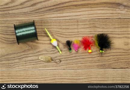 Horizontal top view photo of fishing flies, spoon, float and spool of line on faded wood
