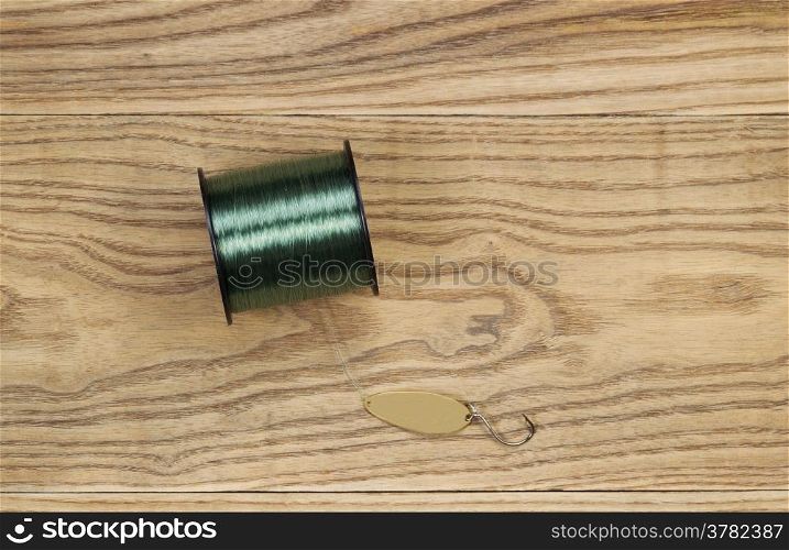 Horizontal top view photo of fishing lure, flat painted metal golden spoon and spool of line on faded wood