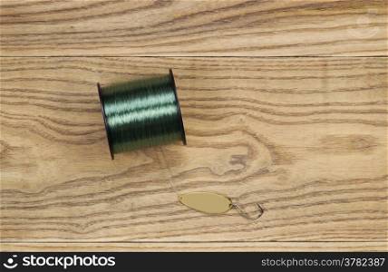 Horizontal top view photo of fishing lure, flat painted metal golden spoon and spool of line on faded wood