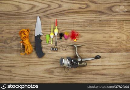 Horizontal top view photo of fishing lures, bobbers, sinkers, hooks, knife, reel and stringer on faded wood