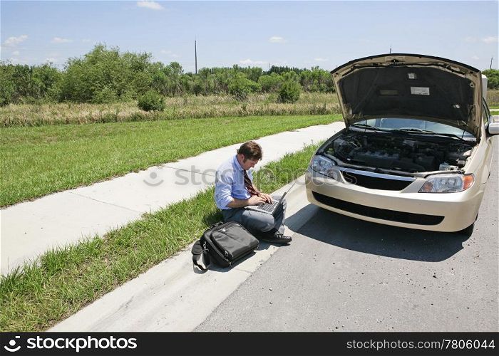 Horizontal view of a man working by the side of the road next to his broken down car.