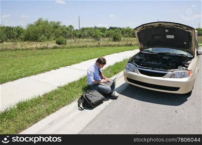 Horizontal view of a man working by the side of the road next to his broken down car.