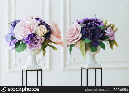 Horizontal view of beautiful artificial flowers in pink and purple colours in white vases on stands in hall for wedding ceremony. Floral decoration