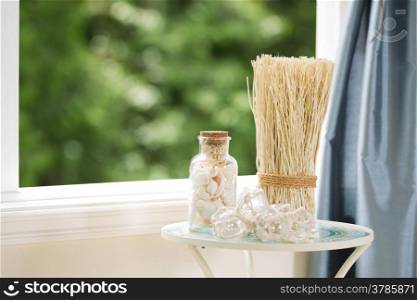 Horizontal view of home decorations on small table next to open window with blurred out green trees in background during bright daylight
