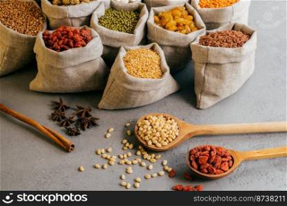 Horizontal view of small sacks with various colorful dry ingredients, two wooden spoons and star anise near. Healthy dieting concept
