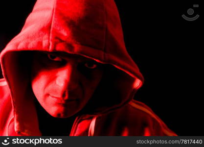 Horror portrait of a hooded man, lit by a red strobe from the side.