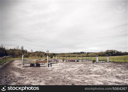 Horse riding track with jump hurdles in an arena with sand in dark cloudy weather