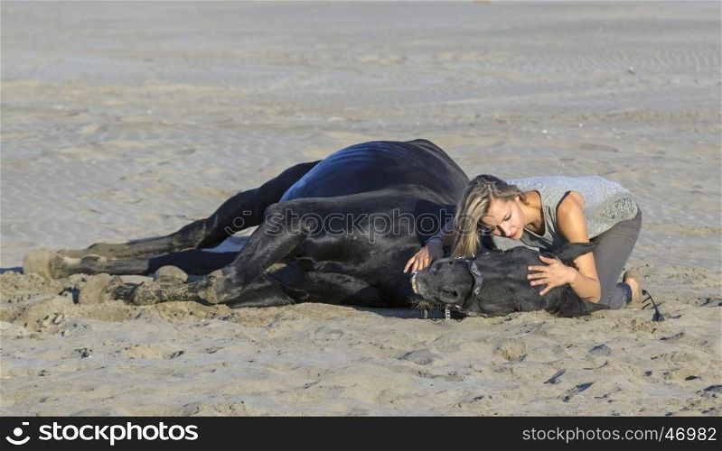 horsewoman and her black stallion laid down on the beach