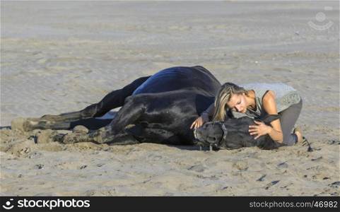 horsewoman and her black stallion laid down on the beach