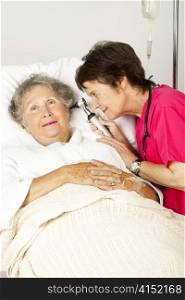 Hospital nurse checking a senior woman patient&rsquo;s ears with an otoscope.