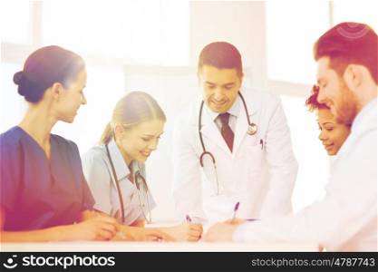 hospital, profession, people and medicine concept - group of happy doctors meeting and taking notes at medical office