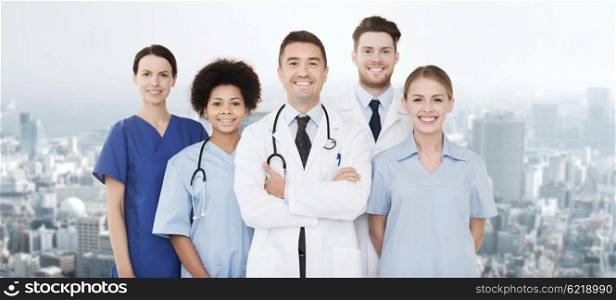 hospital, profession, people and medicine concept - group of happy doctors over city background