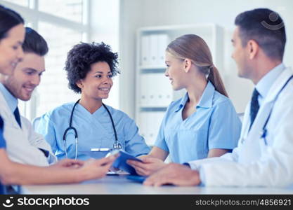 hospital, profession, people and medicine concept - group of happy doctors with tablet pc computers meeting at medical office