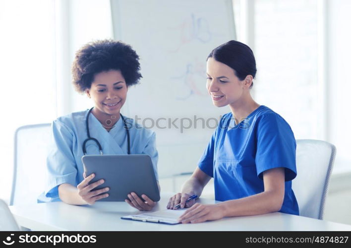 hospital, profession, people and medicine concept - group of happy doctors with tablet pc computer and clipboard meeting at medical office