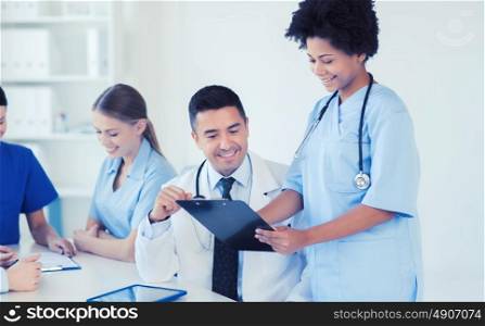 hospital, profession, people and medicine concept - group of happy doctors with clipboard meeting and discussing something at medical office. group of happy doctors meeting at hospital office