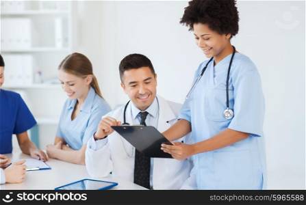 hospital, profession, people and medicine concept - group of happy doctors with clipboard meeting and discussing something at medical office