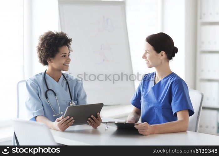 hospital, profession, people and medicine concept - group of happy doctors with tablet pc computer and clipboard meeting at medical office