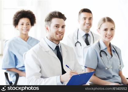hospital, profession, people and medicine concept - group of happy doctors with clipboard on seminar in lecture hall at hospital