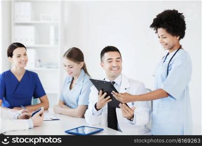 hospital, profession, people and medicine concept - group of happy doctors with clipboard meeting and discussing something at medical office