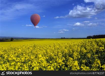Hot air balloon drifting over field of oilseed rape in the Harwardian Hills in North Yorkshire in the northeast of England.