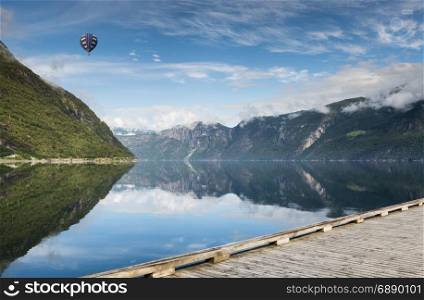 hot air balloon flying over the mountains and in fjord in norway with wooden walking track in front