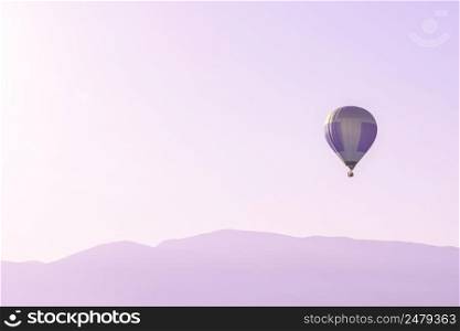 Hot air balloon in the pink sky above soft sunrise mountains silhouettes with copy space