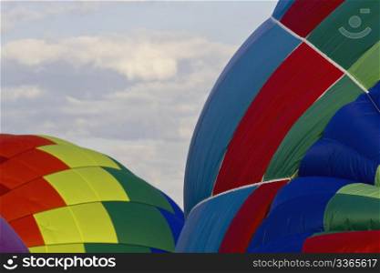 Hot air balloons, still soft, are slowly inflated in the early morning with colorful panels creating spherical patterns with copy space in cloud-filled sky; New Jersey Festival of Ballooning;
