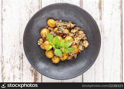 hot and spicy stir fried chicken ovary egg with chicken entrails, offal, pluck, variety meats, organ meats and basil in dark plate on white wood texture background, top view, Thai local street food