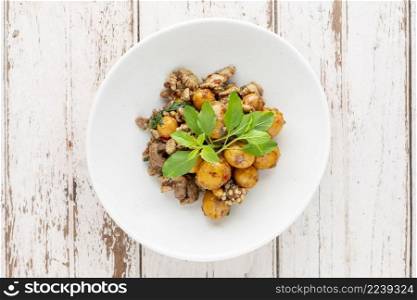 hot and spicy stir fried chicken ovary egg with chicken entrails, offal, pluck, variety meats, organ meats and basil in white plate on white wood texture background, top view, Thai local street food
