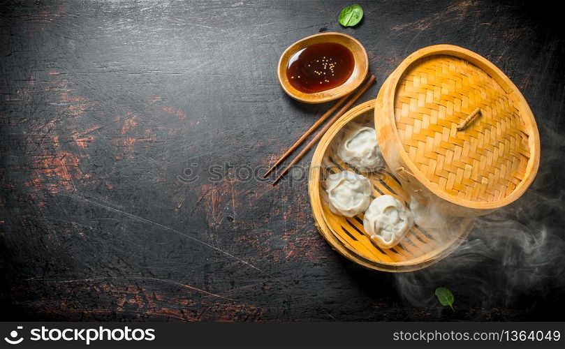Hot aromatic manta dumplings in bamboo steamer with soy sauce. On dark rustic background. Hot aromatic manta dumplings in bamboo steamer with soy sauce.