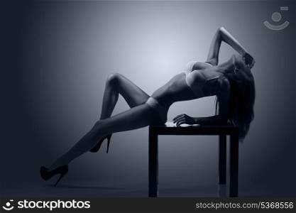 hot backlight portrait of alluring girl posing on small table with sexy white lingerie showing her perfect body