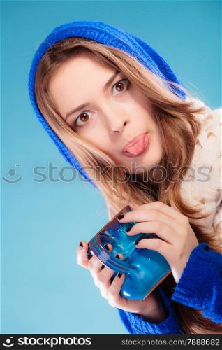 Hot beverage. Closeup funny teen girl holding blue mug with drink tea or coffee. Woman having fun, making silly face sticking tongue