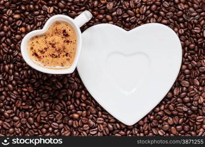 Hot beverage. White coffee cup heart shaped with cappucino latte on roasted beans background