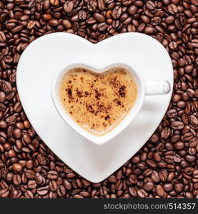 Hot beverage. White coffee cup heart shaped with cappucino latte on roasted beans background