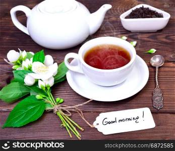 hot black tea in a white cup with a saucer, behind a white tea pot