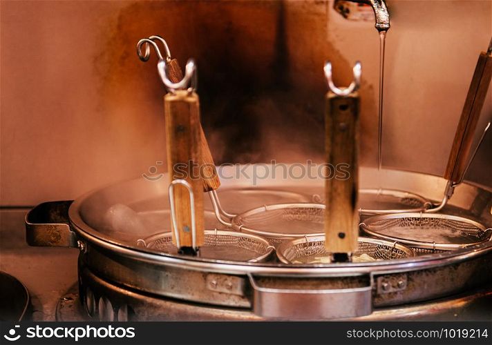 Hot boiling Ramen pot with noodle strainers and steam close up shot of Ramen noodle restaurant with warm tone light. Selective focus