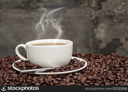 Hot breakfast coffee cup and saucer surrounded by coffee beans on rustic background