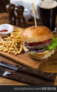 hot burger serving on wooden board with dark beer in restaurant