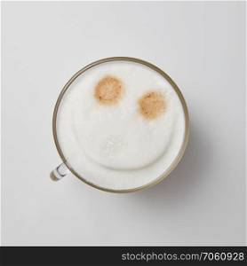 Hot cappuccino in a glass cup with a smile face on a gray background with space for text. Top view. A cup of fragrant cappuccino with a smile face on a gray background with a copy of the space. Top view