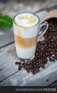 Hot caramel coffee in glass with coffee beans on wooden table background.