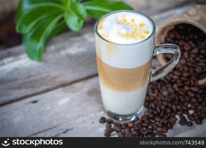 Hot caramel coffee in glass with coffee beans on wooden table background.