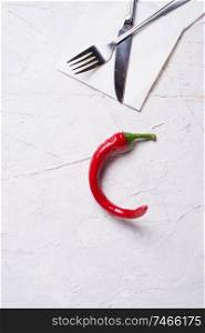 hot chili pepper with fork and knife at white table. copy space. flat lay