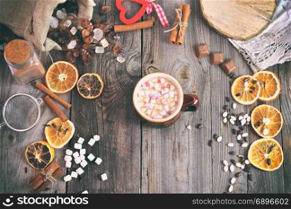 hot chocolate in a mug with marshmallow on a gray wooden table in the middle of sweets, top view