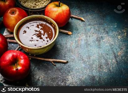 Hot chocolate in bowl and red apples with twigs , ingredients for sweet apples making, preparation on rustic background, close up