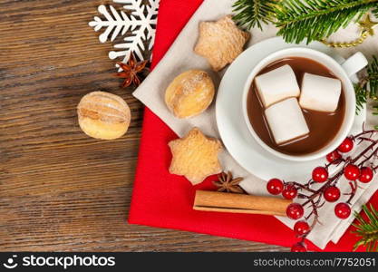Hot chocolate or cocoa drink in a white cup, sweet homemade cookies and cinnamon on a brown wooden background. Christmas and new year traditional food. Top view